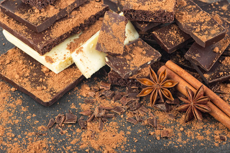 Broken chocolate pieces, cocoa powder, cinnamon sticks and anise stars on a black backgroundの写真素材