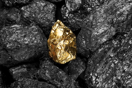 Shiny golden nugget on black coals, top view.の写真素材
