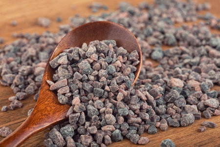 Himalayan black rock salt in wooden spoon on rustic background, volcanic salt. Traditional seasoning in the culinary arts of India, Nepal, Bhutan, Bangladesh.の写真素材