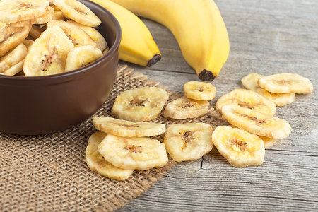 Healthy Food - dried banana slices and fresh bananas on wooden table. Banana chips.の写真素材