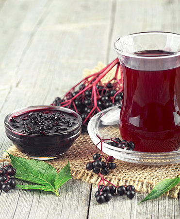 Homemade black elderberry syrup in glass jar and bunches of black elderberry on wooden tableの写真素材