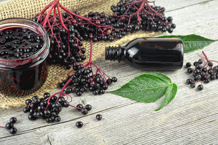 Black elderberry fruit on vintage wooden board, Sambucus. Branches of elderberry with green leaves, elderberry jam, syrup and confiture. European black elderberry. Alternative medicine and lifestyle.の写真素材