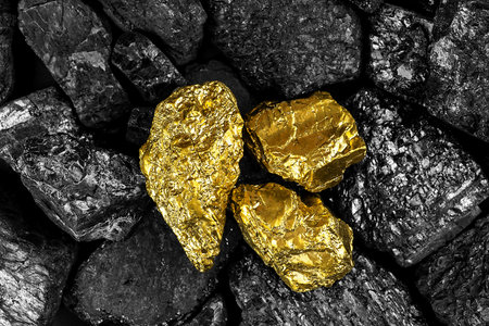 Shiny gold nuggets on black coals, view from above. Pieces of gold among the coal.の写真素材