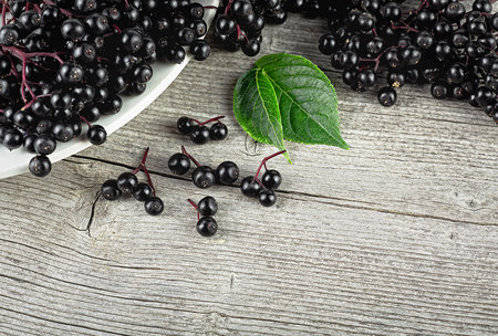 Fresh black elderberries with green leaves on wooden desk, top view. European black elderberry, Sambucus.の写真素材