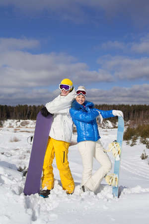 Pretty couple with snowboards in their hand standing on a hillside, sunny winter dayの写真素材