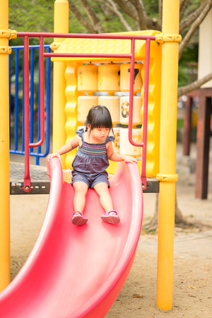 Asian little girl enjoys playing slider in a children playgroundの写真素材