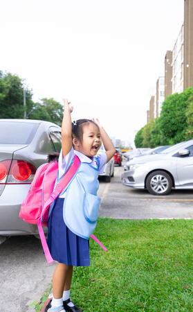 happy little girl with backpack jumping in car park ready back to schoolの写真素材