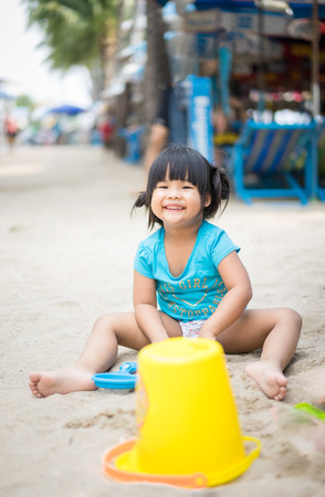 smiling little girl playing sand on the beachの写真素材