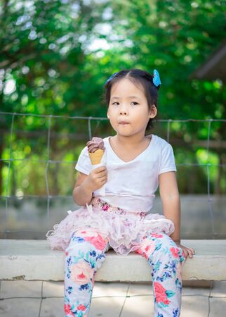 Asian little girl eating an ice cream outdoors with natural light blur backgroundの写真素材