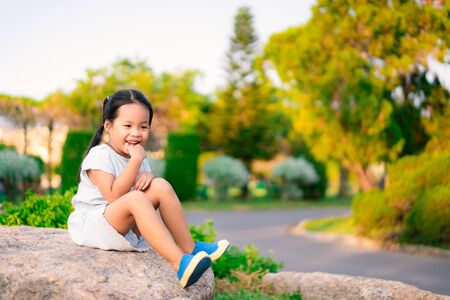 Beautiful little smiling girl sitting outdoors on large rockの写真素材