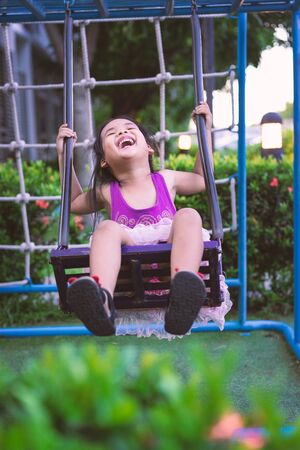 Asian little girl enjoys playing swing in a children playgroundの写真素材