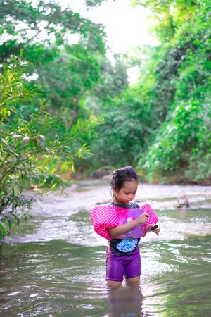 little asian girl wearing inflatable sleeves playing in nature water on holidayの写真素材