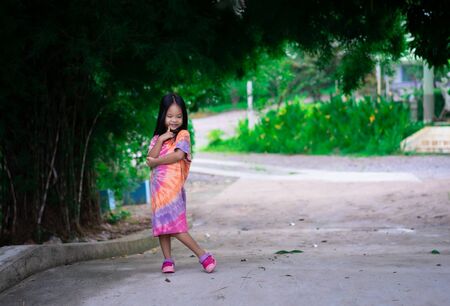 Portrait of happy asian little girl in dress standing on footpath in the parkの写真素材
