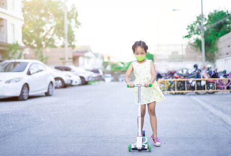Cute little asian girl wearing a mask against dust and virus while learning to ride a scooterの写真素材