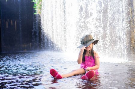 happy little asian girl wear hat playing waterfall on holidayの写真素材