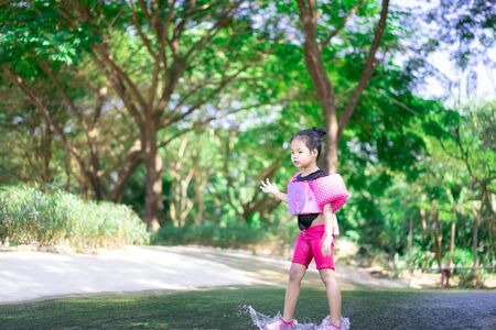 little asian girl wearing inflatable sleeves playing water in nature water on holidayの写真素材