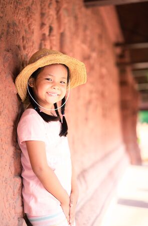 Portrait of little asian girl wearing hat standing near the wallの写真素材