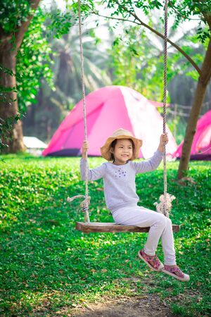 Little girl in pink dress sitting on a swing while campingの写真素材