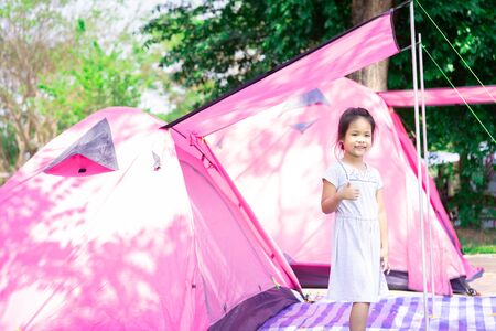 Portrait of little asian girl standing with tents while going campingの写真素材