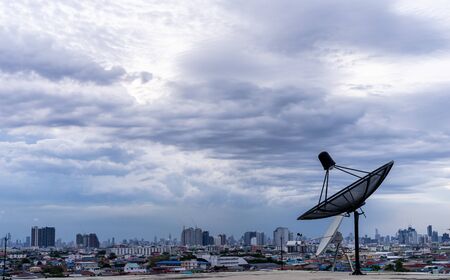 Satellite dish antenna on top of the building in urban and cloudy skyの写真素材