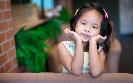 Portrait of little asian smiling girl in yellow dress sitting on a couchの写真素材
