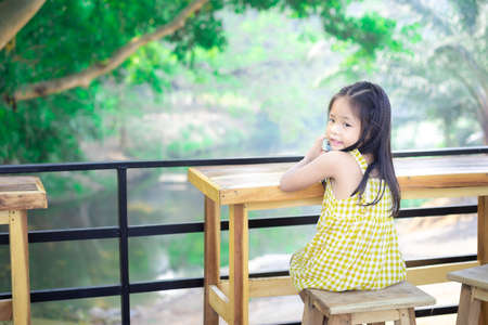 little asian girl sitting on the chair at wooden table on outside restaurantの写真素材