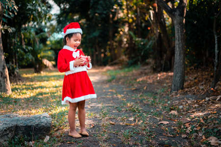 little asian girl in red Santa Claus costume feel surprise with present box in the parkの写真素材