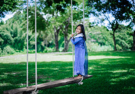 little asian girl in princess costume playing wooden swing in the parkの写真素材