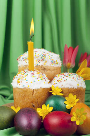 Colored eggs and Easter cakes with a lighted candle on a background of green tissue