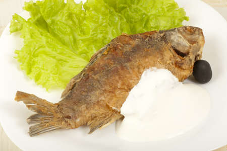 Fish fried carp with sour cream on a plate with lettuce leaves