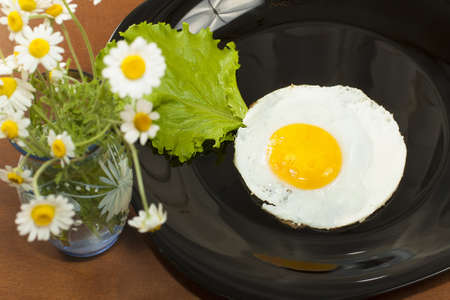 scrambled egg on a black plate and a bunch of daisiesの写真素材