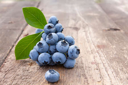 beautiful blueberries with green leaves on an old wooden tableの写真素材