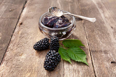 large ripe blackberries and blackberry jam on an old wooden table and a silver spoonの写真素材