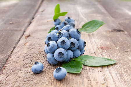 beautiful blueberries with green leaves on an old wooden tableの写真素材