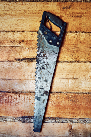 The hand iron rusty saw hangs on a nail.Wood texture. background old panels.の写真素材