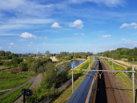 Railway track and speeding train with nature compensation and wind turbines producing green energyの写真素材