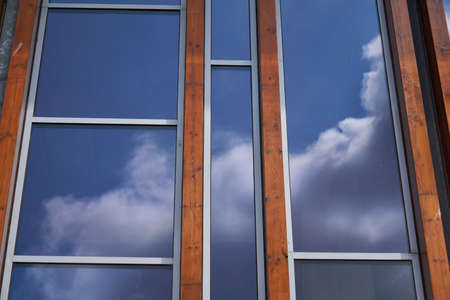 Facade with glass and tropical hardwood reflecting vibrant blue sky with cloudsの写真素材