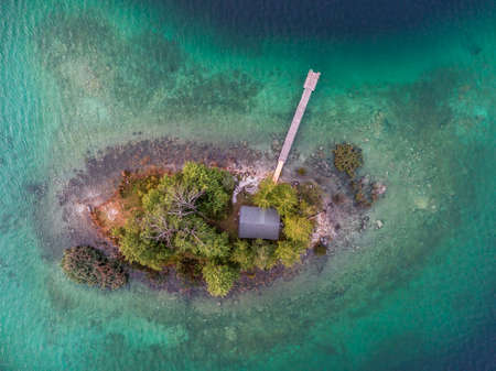 Top down aerial view on tropical island with small cabin surrounded by trees and jetty in lake Eibsee, Germanyの写真素材