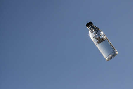 Transparent plastic bottle with water and air bubbles floating in the sunlight on a blue sky plain background with copy spaceの写真素材