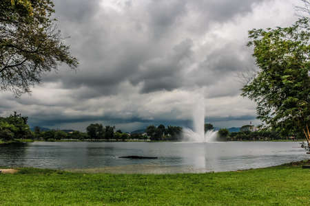 Massive rain clouds over the city pond with fountain.の写真素材