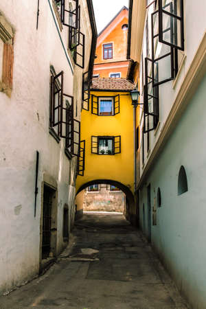 Narrow european street, open shutters in windows and yellow house between.の写真素材