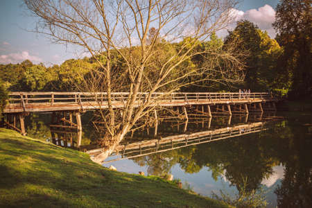 Old wooden bridge is reflected in the clear river.の写真素材