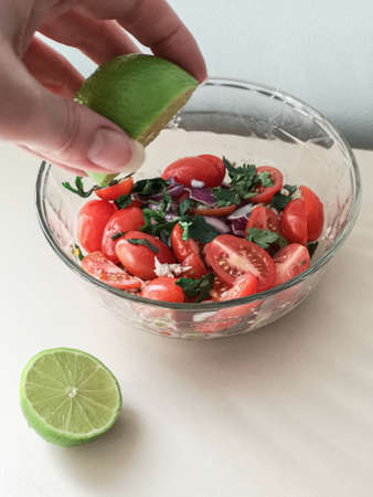 hand squeezes lime juice into tomato, onion, tuna and green saladの写真素材