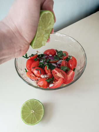 hand squeezes lime juice into tomato, onion, tuna and green saladの写真素材