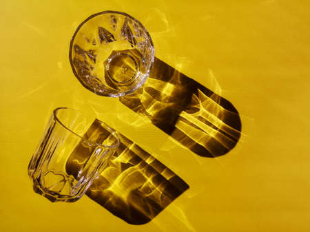 Two glass glasses with faces on a yellow background in hard light with shadowsの写真素材