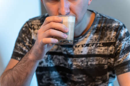 A man drinks cappuccino from a glass sitting at homeの写真素材