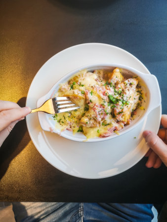 A man eats baked dumplings with a sauce of bacon, ham, herbs and cheese