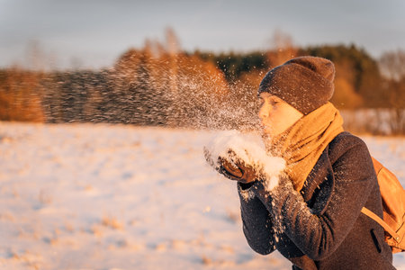 A woman blows a handful of snow from her hands at sunset in the evening.の写真素材
