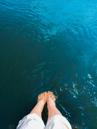 A woman lowered her feet into turquoise seawaterの写真素材