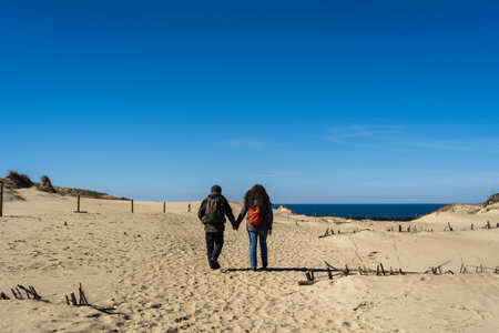 A couple of travelers with a backpack, hand in hand, walks along the sandy Dead Dunes, on the Curonian Spit, on the shore of the Baltic Seaの写真素材